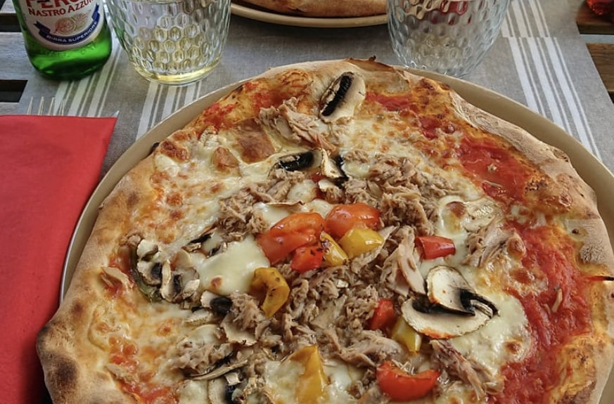 Pizza garnie et bière Peroni sur table.